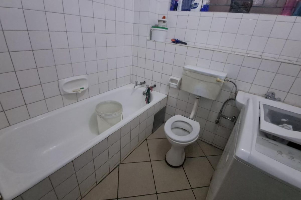 A functional bathroom featuring a standard bathtub, toilet, and tiled walls, requiring cosmetic updates to modernize the space.