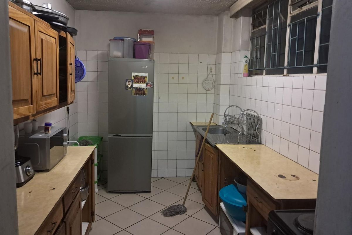 A functional kitchen featuring wooden cabinetry, tiled walls, and a stainless steel sink, offering a practical layout with potential for modernization.