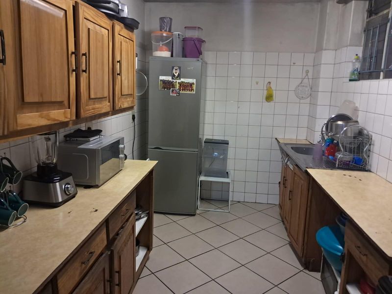 A functional kitchen featuring wooden cabinetry, tiled walls, and tiled flooring, providing a practical workspace with integrated sink and storage.