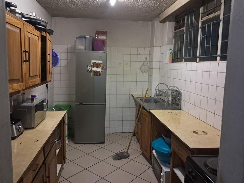 A functional kitchen featuring wooden cabinetry, tiled walls, and a stainless steel sink, offering a practical layout with potential for modernization.