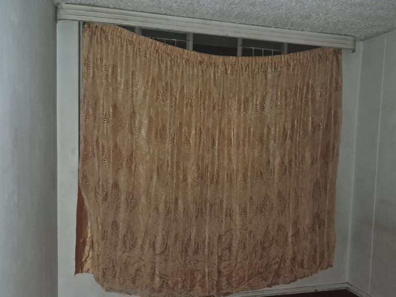A bedroom interior featuring a window with a curtain track and textured ceiling, showing signs of wear and requiring cosmetic updates.
