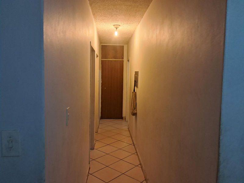 A narrow interior hallway featuring tiled flooring and a simple ceiling light fixture, providing access to adjacent rooms.
