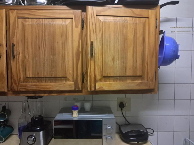 A kitchen area featuring dated wooden cabinetry and white tiled splashbacks with visible wear.