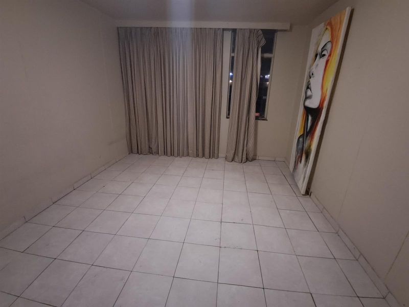 An empty living room featuring tiled flooring and full-length curtain tracks, providing a blank canvas for potential interior design updates.