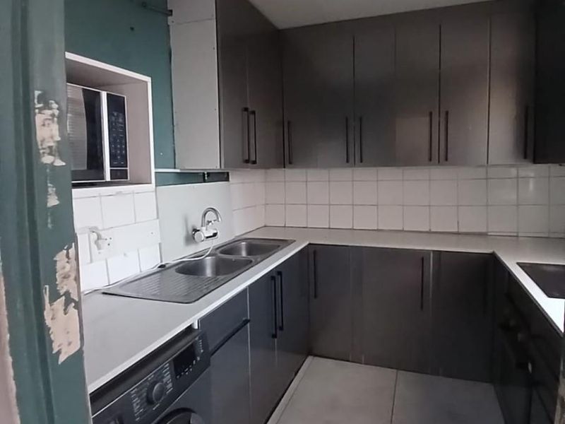 Compact kitchen featuring dark cabinetry, tiled backsplash, integrated appliances, and exposed plumbing, requiring cosmetic updates to improve overall finish and aesthetic appeal.