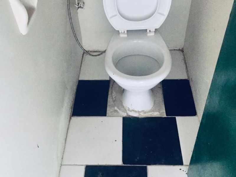 A small bathroom featuring a toilet with a checkered tile floor, requiring maintenance and cosmetic updates to improve its overall condition.