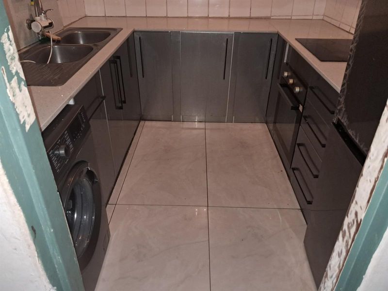 Compact kitchen featuring modern grey cabinetry, integrated oven and hob, double bowl sink, and tiled flooring with a neutral backsplash.