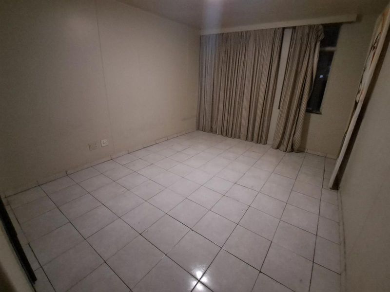 An empty bedroom featuring tiled flooring and full-length curtain tracks, providing a blank canvas for personalization.