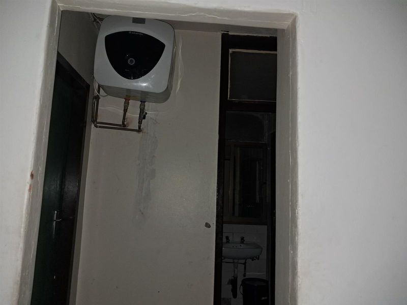 A utility area featuring a wall-mounted electric water heater with visible signs of wall moisture damage and peeling paint.