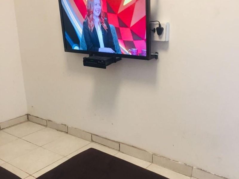 A living area featuring tiled flooring and a wall-mounted television setup with visible wear on the skirting boards and wall finishes.