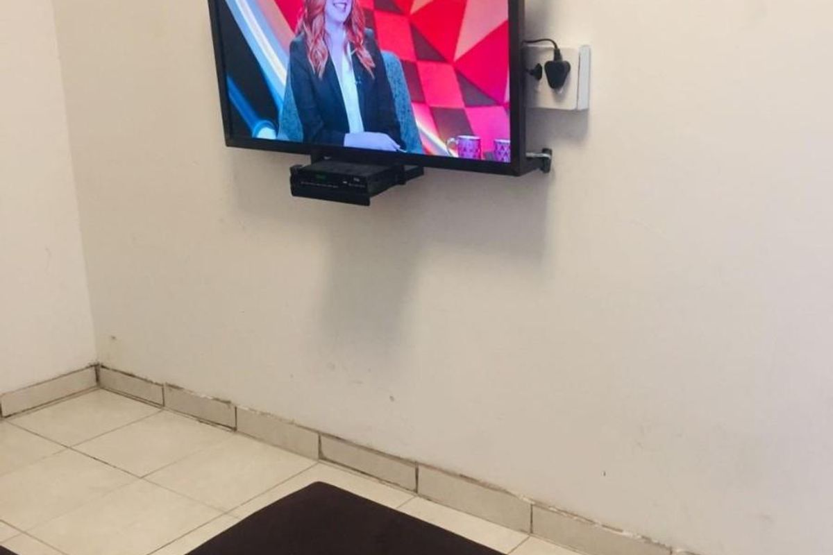 A living area featuring tiled flooring and a wall-mounted television setup with visible wear on the skirting boards and wall finishes.