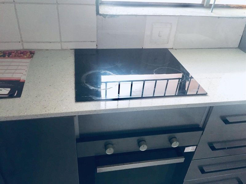 A compact kitchen area featuring a built-in oven, electric hob, stone countertops, and tiled backsplash, ready for modern updates.