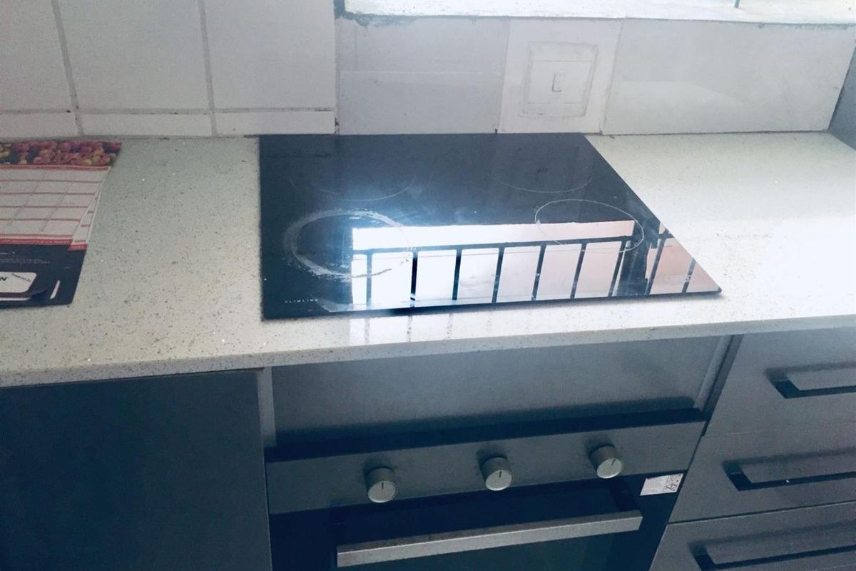 A compact kitchen area featuring a built-in oven, electric hob, stone countertops, and tiled backsplash, ready for modern updates.