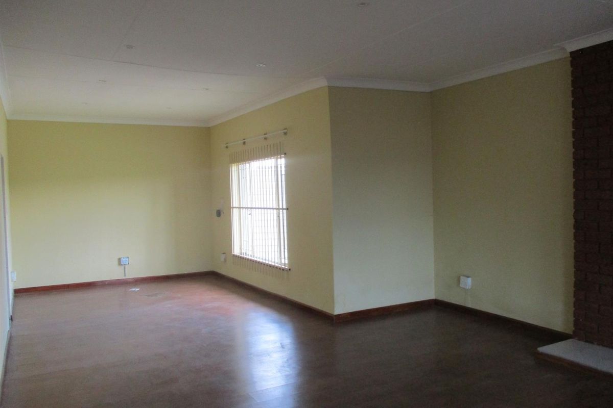 Spacious, empty living room featuring a brick fireplace, laminate flooring, and neutral wall finishes, offering a blank canvas for interior design.