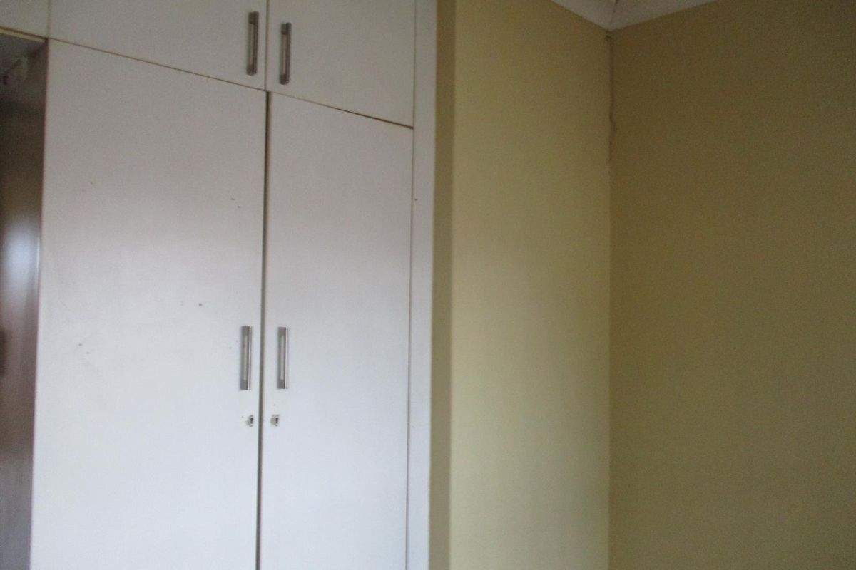 A bedroom corner featuring built-in white cupboards with metal handles and yellow painted walls showing signs of wear.