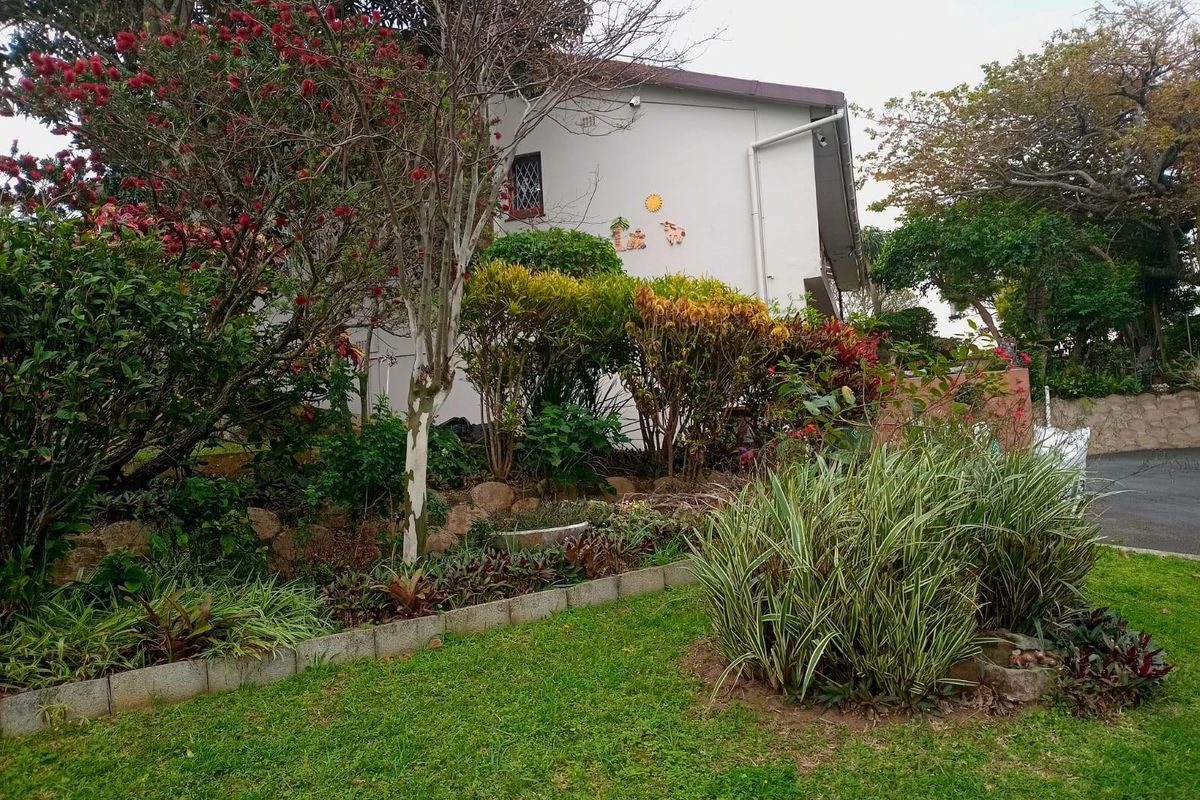 A view of the side exterior of the house featuring a landscaped garden with established shrubs, trees, and a lawn area.
