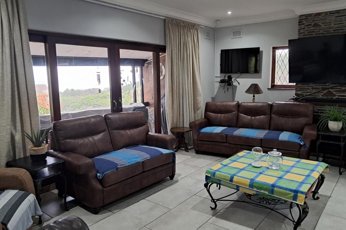 A comfortable living room featuring large sliding glass doors leading to an outdoor area, tiled flooring, and a stone-clad fireplace feature wall.