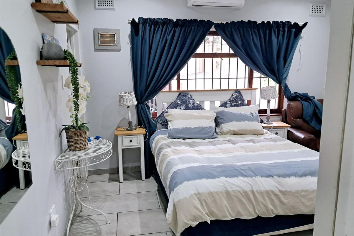 A well-maintained bedroom featuring tiled flooring, a wall-mounted air conditioning unit, and security bars on the window.