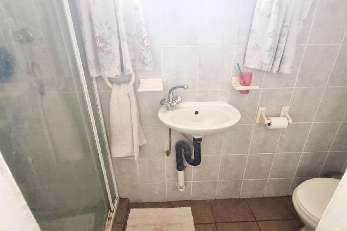 Compact bathroom featuring a wall-mounted basin, shower enclosure, and toilet with tiled walls and flooring.