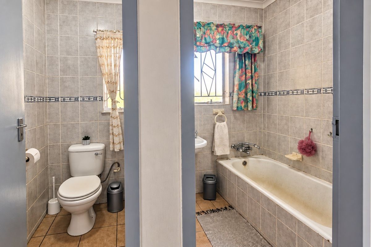 A dated bathroom featuring a separate toilet and bathtub area with tiled walls and floors, requiring cosmetic updates to modernize the space.