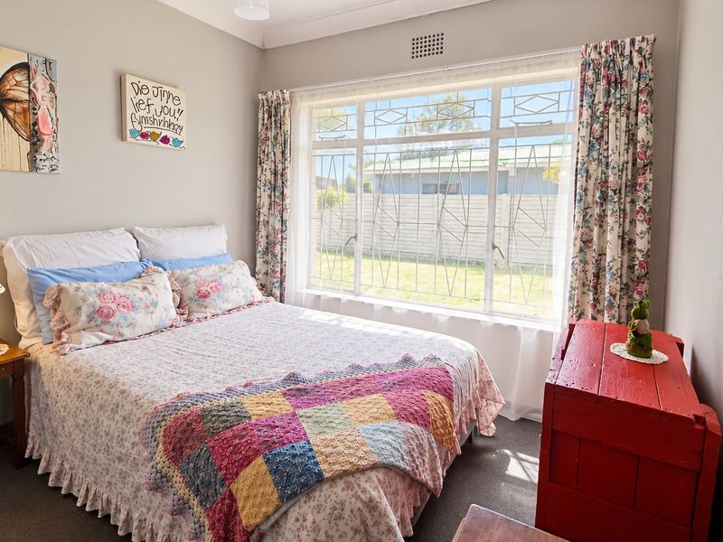 A cozy bedroom featuring a large window with security bars, providing natural light and a view of the rear garden area.