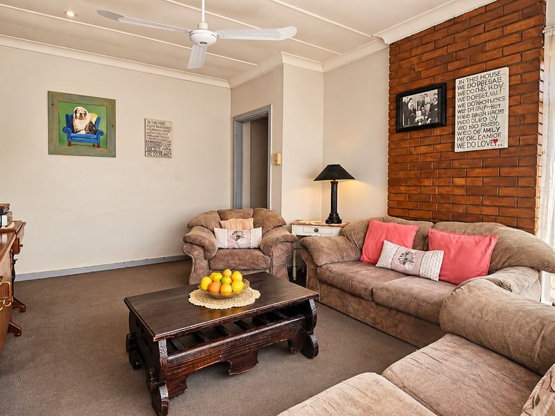 A comfortable living room featuring an exposed brick accent wall, ceiling fan, and large sliding glass doors providing natural light.