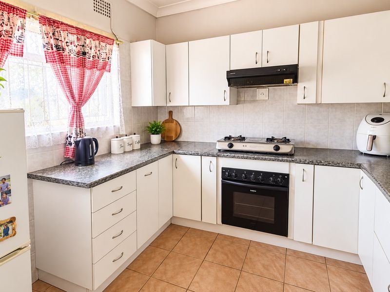 A functional kitchen featuring white cabinetry, granite-look laminate countertops, a gas hob with extractor fan, and tiled flooring.