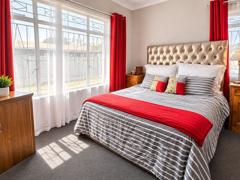 A well-lit bedroom featuring large windows with security bars, carpeted flooring, and decorative coving, providing a comfortable and functional sleeping space.