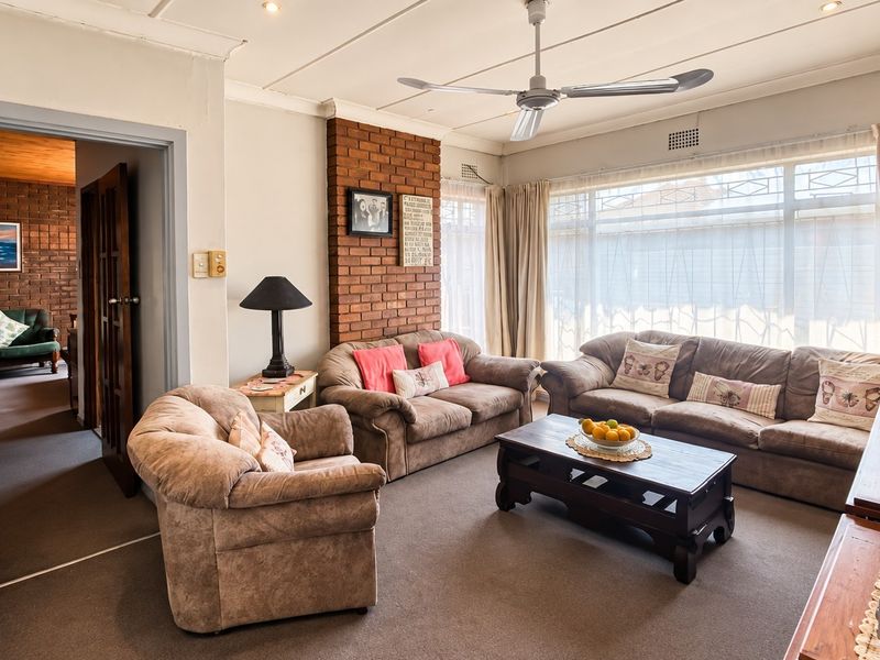 A comfortable living room featuring an exposed brick fireplace, ceiling fan, and large windows that provide ample natural light.