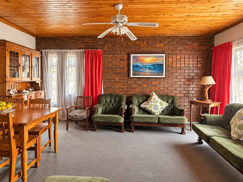 A living room featuring an exposed brick feature wall, timber ceiling, and ceiling fan, offering a traditional aesthetic with potential for modern updates.