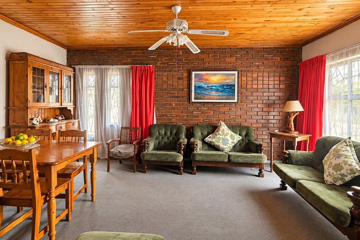 A living room featuring an exposed brick feature wall, timber ceiling, and ceiling fan, offering a traditional aesthetic with potential for modern updates.