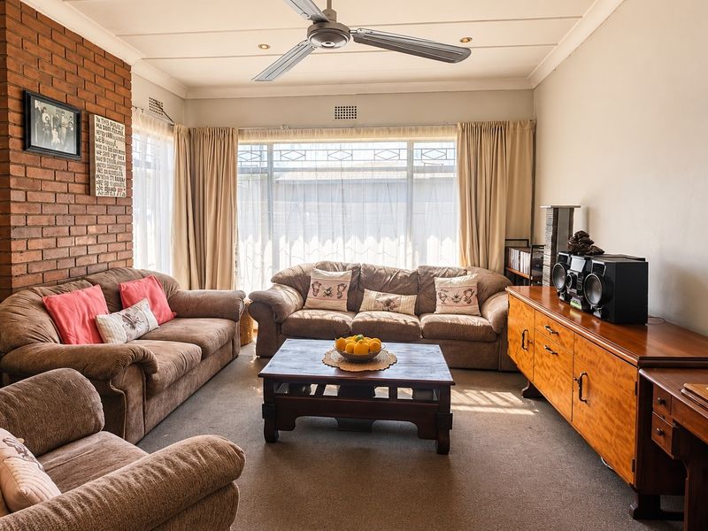A comfortable living room featuring an exposed brick fireplace, ceiling fan, and large windows that provide ample natural light.