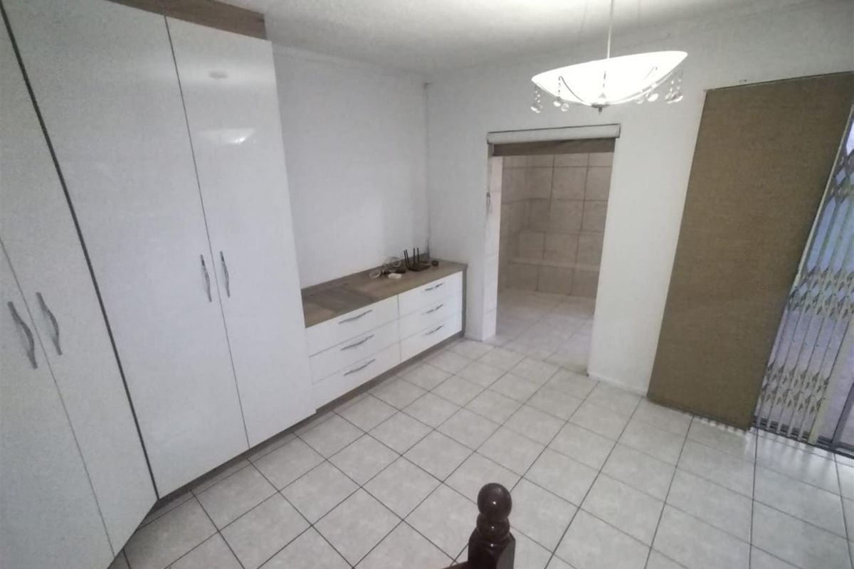 A functional bedroom featuring built-in white cabinetry, tiled flooring, and a neutral layout with direct access to an adjoining bathroom area.