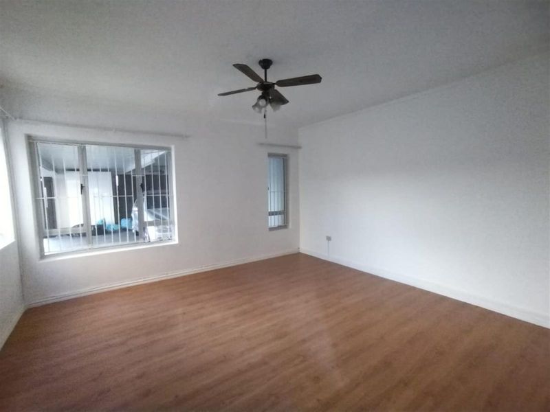 A bright, empty living room featuring wood-look laminate flooring, a ceiling fan, and security bars on the windows.