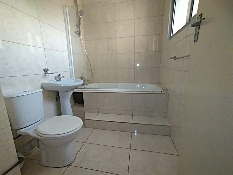 A functional bathroom featuring a pedestal basin, a toilet, and a tiled bathtub with a shower mixer.