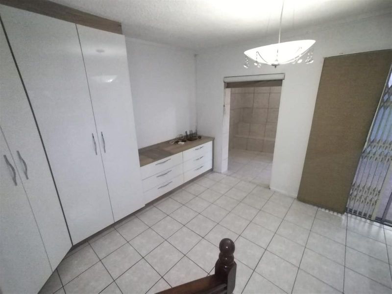 A functional bedroom featuring built-in white cabinetry, tiled flooring, and a neutral layout with direct access to an adjoining bathroom area.