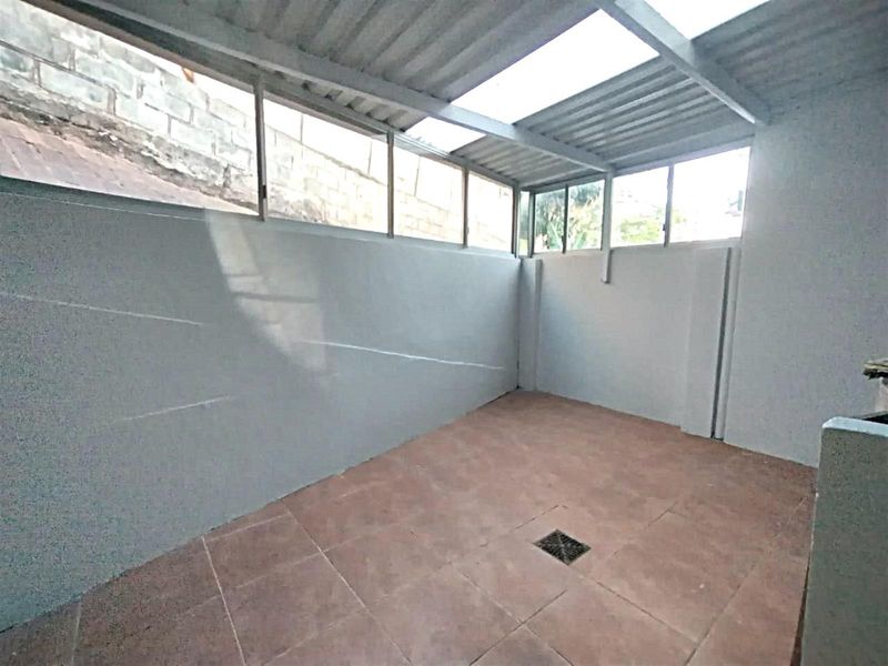 A covered outdoor utility or patio area featuring tiled flooring, a corrugated roof with skylight panels, and perimeter windows.
