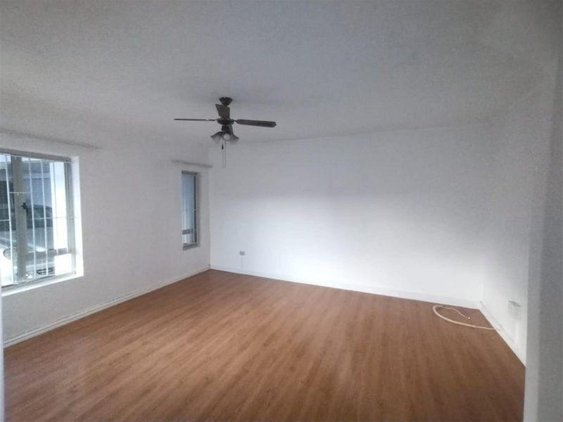 A spacious, empty living room featuring wood-look laminate flooring, white walls, and a ceiling fan, offering a blank canvas for personalization.