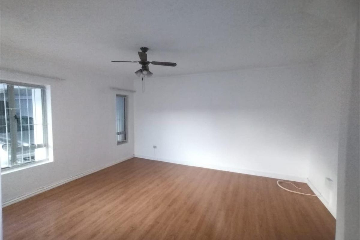 A spacious, empty living room featuring wood-look laminate flooring, white walls, and a ceiling fan, offering a blank canvas for personalization.