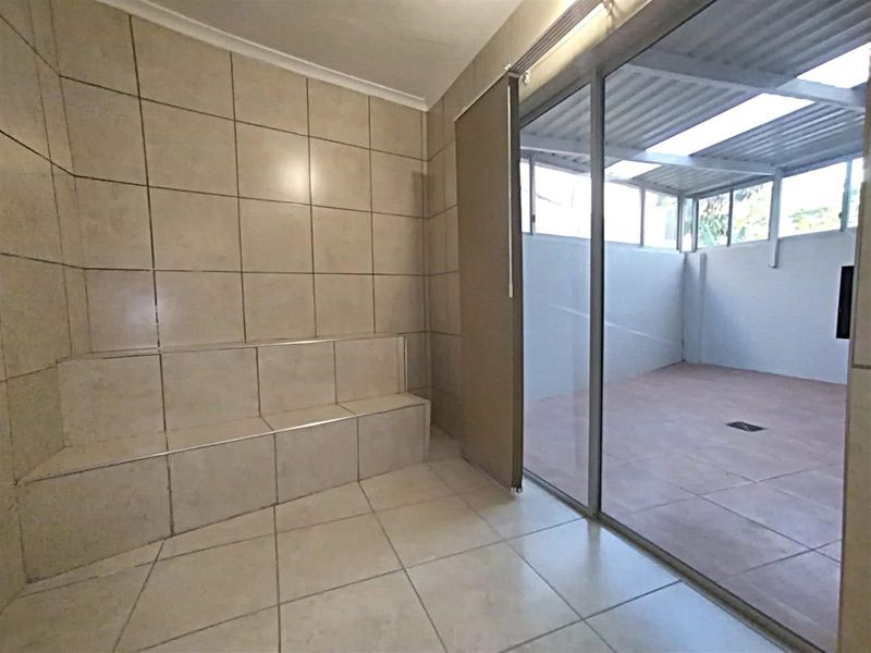 A tiled interior space featuring a built-in tiled bench, leading through sliding glass doors to a covered outdoor patio area.