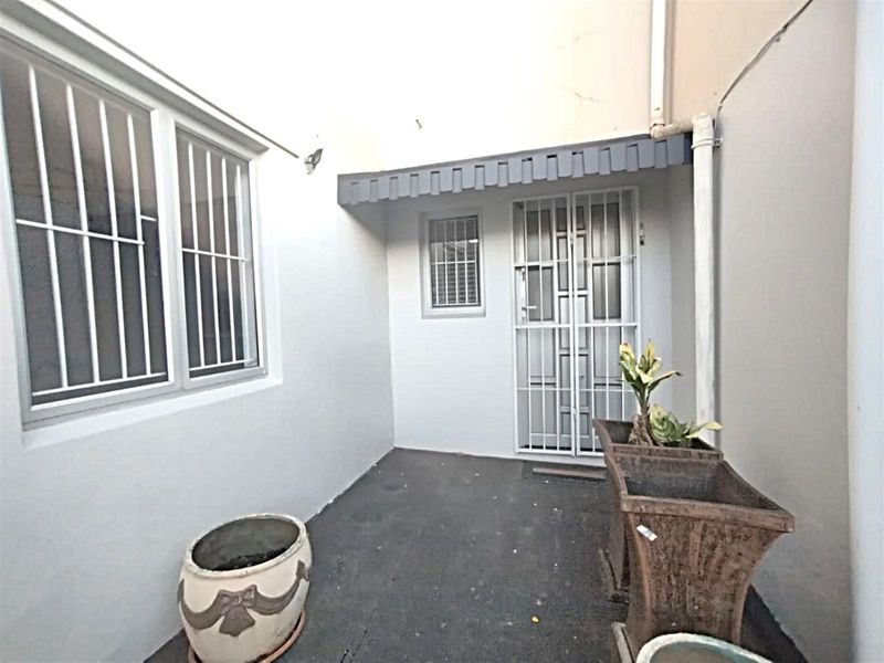 A compact, paved rear courtyard area featuring security gates, window bars, and a small protective awning over the entrance.
