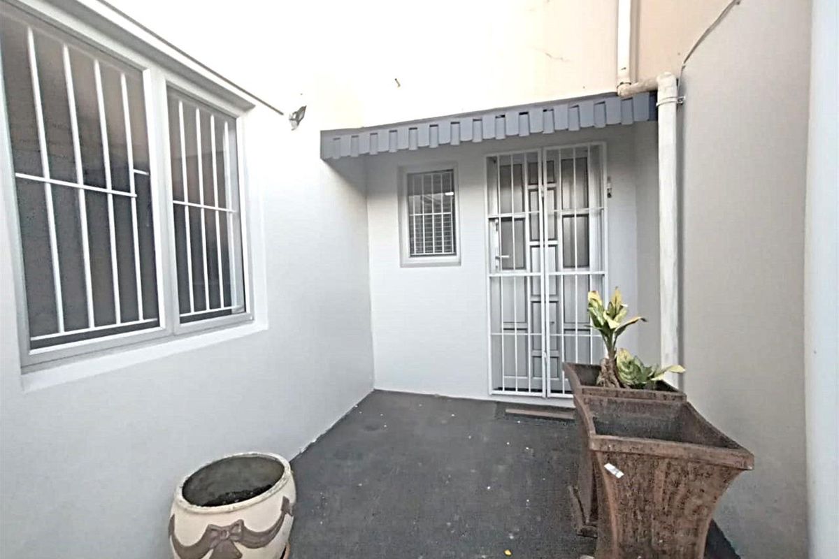 A compact, paved rear courtyard area featuring security gates, window bars, and a small protective awning over the entrance.