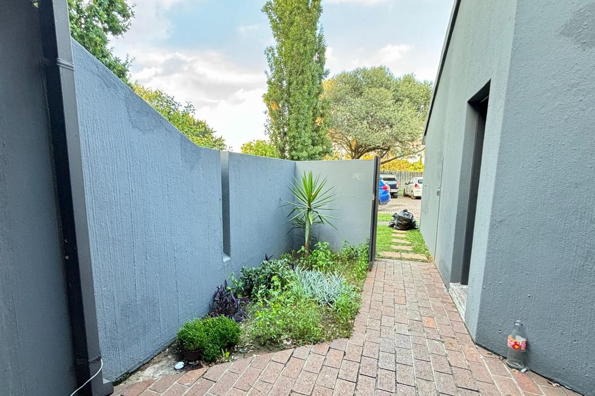 A side walkway featuring brick paving, a painted boundary wall, and a downpipe, leading towards the rear garden area.