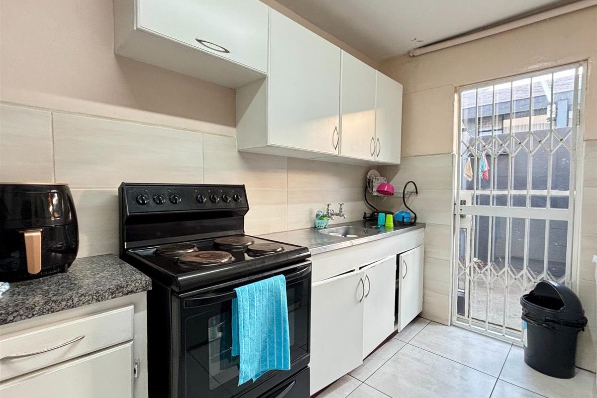 Compact kitchen featuring white cabinetry, tiled splashbacks, an electric stove, and direct access to an exterior area through a security gate.
