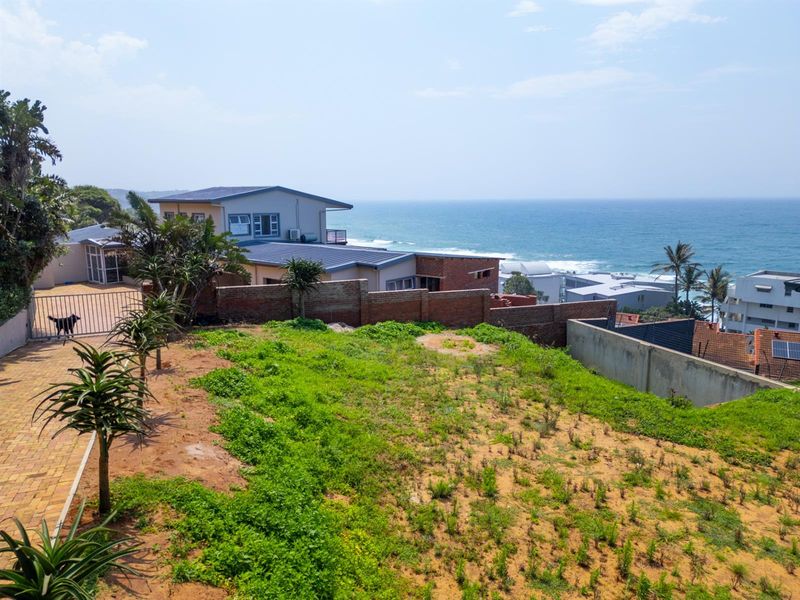 Elevated view of a vacant residential plot featuring a paved driveway, boundary wall, and scenic ocean views.