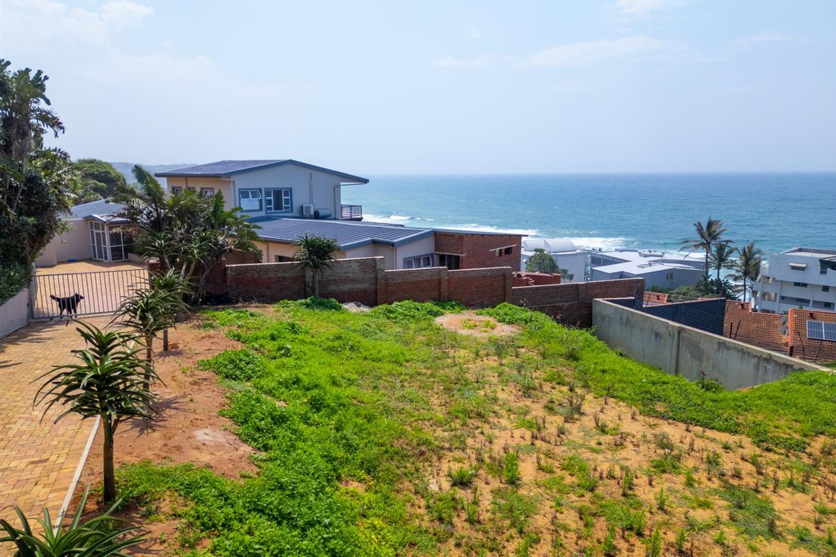 Elevated view of a vacant residential plot featuring a paved driveway, boundary wall, and scenic ocean views.