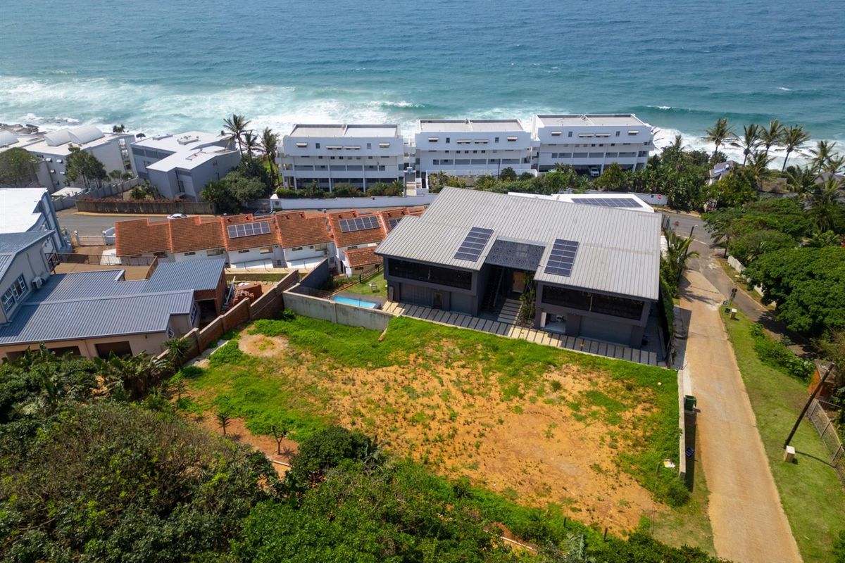 Aerial view of a residential property featuring a modern home with solar panels, situated near the coastline with surrounding neighborhood infrastructure.