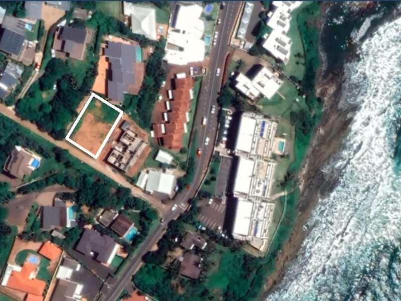 Aerial view of a vacant residential land plot situated in a coastal neighborhood near the ocean.