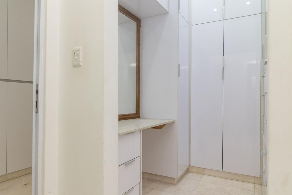 A clean, modern dressing area featuring built-in white cabinetry, a vanity counter, and a wall-mounted mirror.