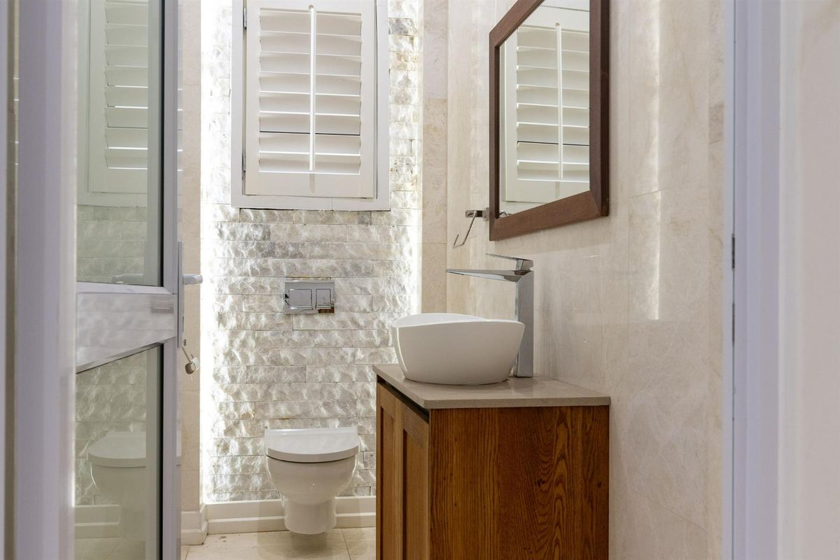Modern bathroom featuring a stone-clad feature wall, wall-mounted toilet, wooden vanity with a vessel sink, and plantation shutters.